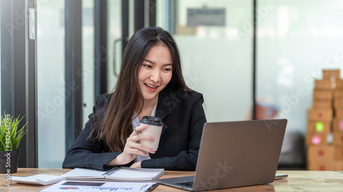 Image of a beautiful Asian businesswoman happy a successful work holding a coffee cup with a laptop and document at the office.