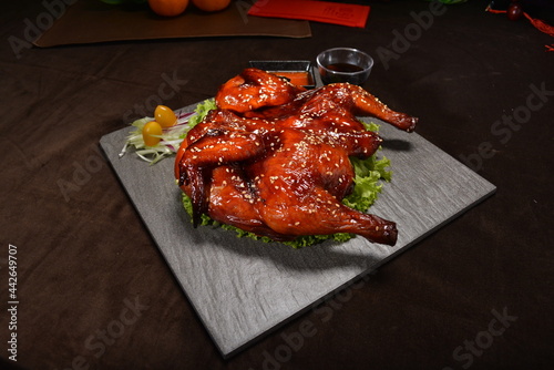 roasted bbq whole chicken in red honey sauce with sesame seed on top black stone plate
