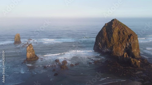 Beautiful Sunrise on the Oregon Coast - Mossy Haystack Rock and Crystal Clear Blue Water Crashing Against the Pacific Ocean Coast, Sea birds flying above 4K 30fps Aerial Drone Footage High Static Shot photo