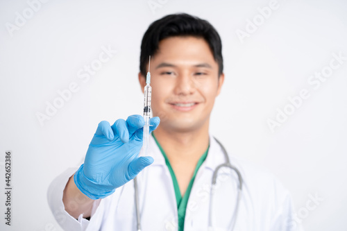 Asian male doctor holding syringe with coronavirus vaccine. He was wearing a protective suit and a mask.