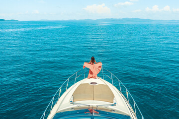 Woman standing on the bow of a yacht on a sunny summer day, breeze of developing hair, beautiful sea on the background
