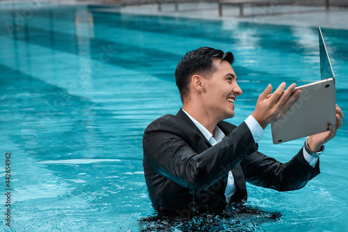 A man in a business suit is ready to drown his laptop while standing in the pool. Bad news. The collapse of prices. Business crash. Failure