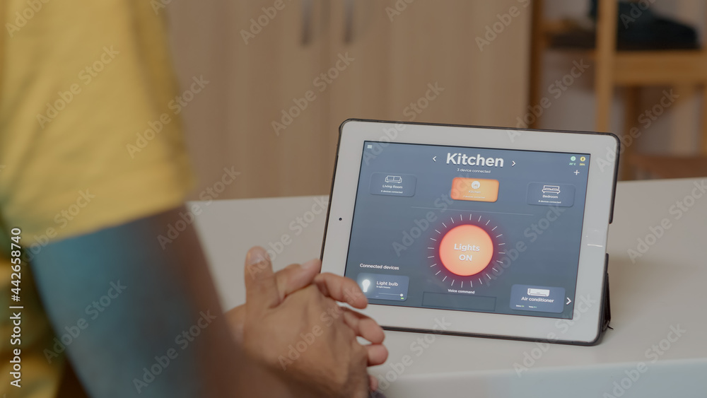 Man using voice activated smart wireless lighting app on tablet turning on the bulbs in house with modern software. Person controlling ambience light with future technology, voice activation command
