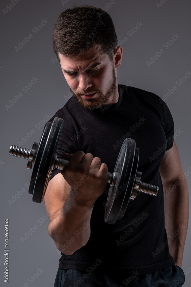 Concentrated young man performing bicep curl with dumbbell