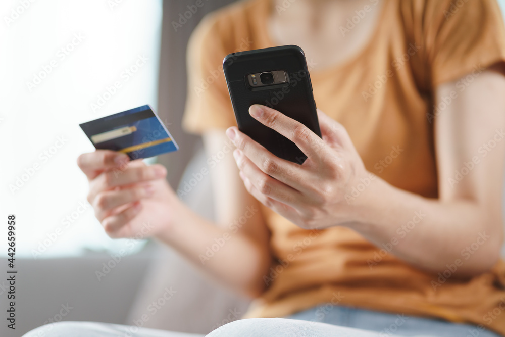 Young woman holding credit card and using smart phone for online shopping, internet banking, e-commerce, spending money, working from home concept Young woman holding credit card and using smart phone for online shopping, internet banking, e-commerce, spending money, working from home concept