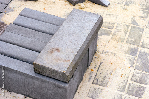 Stack of curbstones on stone tiles in sand.