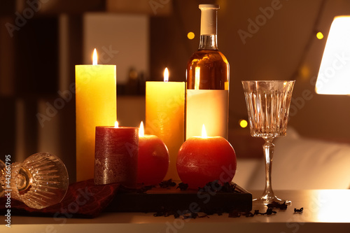 Burning candles and bottle of wine on table in room
