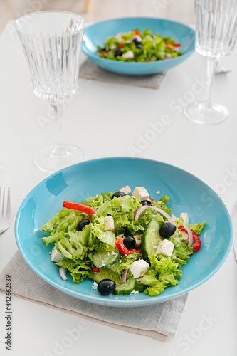 Plates with fresh Greek salad and glasses on table in restaurant