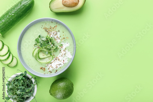 Bowl with green gazpacho and ingredients on color background