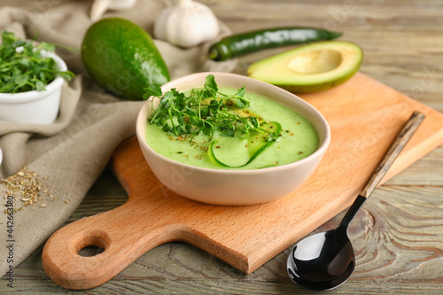 Bowl with green gazpacho and ingredients on wooden background