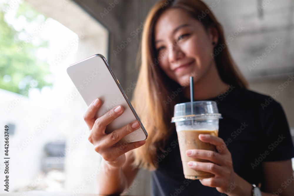 Closeup image of a beautiful young asian woman holding and using mobile phone while drinking coffee in cafe Closeup image of a beautiful young asian woman holding and using mobile phone while drinking coffee in cafe