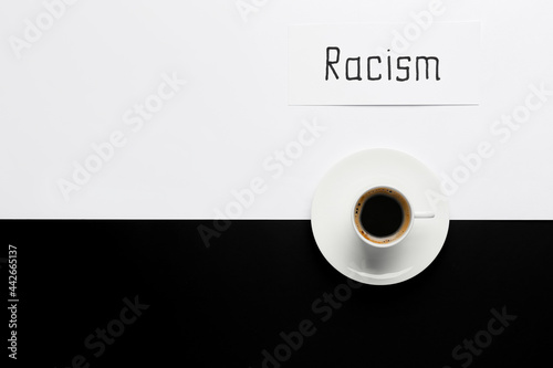 Paper piece with word RACISM and cup of coffee on black and white background