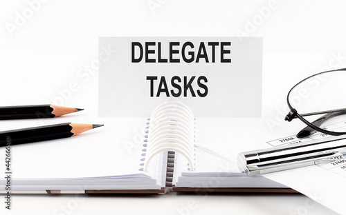 Text DELEGATE TASKS on paper card,pen, pencils, glasses,financial documentation on table - business concept
