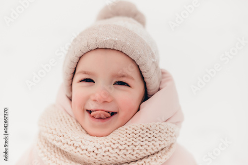 Happy laughing girl wearing a pink jacket, scarf and hat, playing in a beautiful snowy winter walk. Girl enjoys winter, frosty day. Playing with snow on winter holidays. Winter holidays concept.