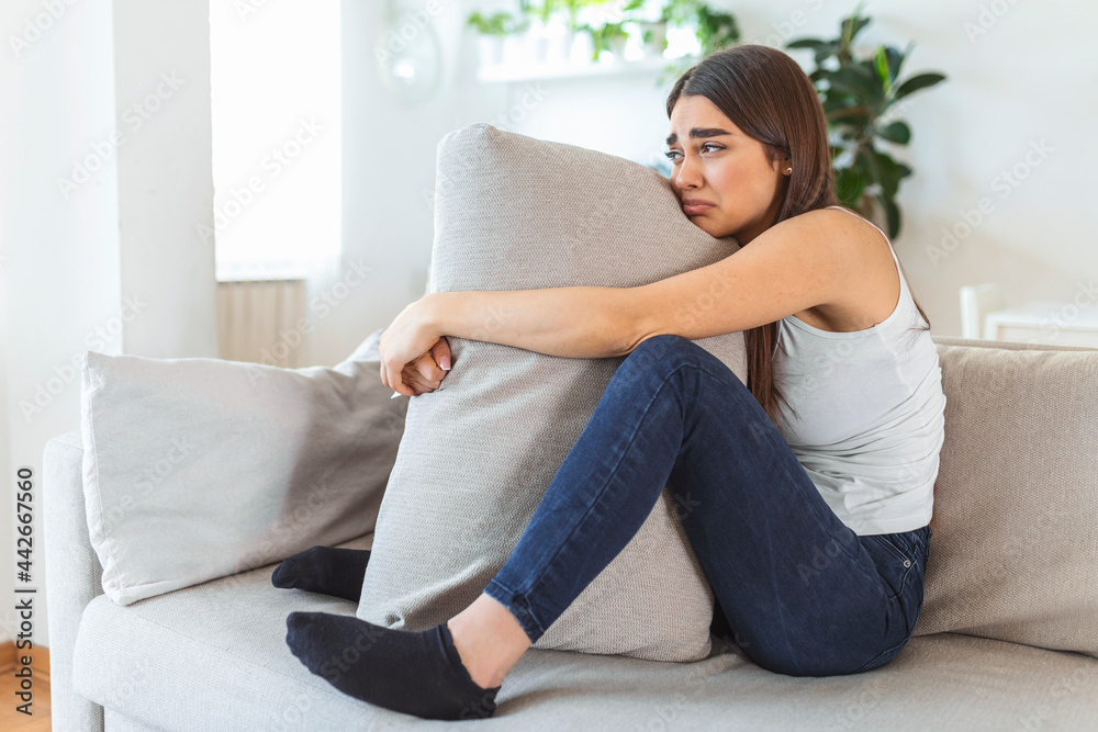 Difficult times. Portrait of a cheerless sad caucasian woman holding her hands crossed and hugging big pillow while thinking about her problems. Stock photo Difficult times. Portrait of a cheerless sad caucasian woman holding her hands crossed and hugging big pillow while thinking about her problems. Stock photo