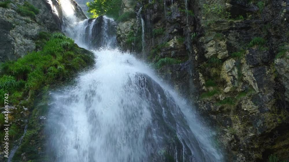 Clear water falling from mountain splashing and foaming on cliffs covered in green lush vegetation Clear water falling from mountain splashing and foaming on cliffs covered in green lush vegetation