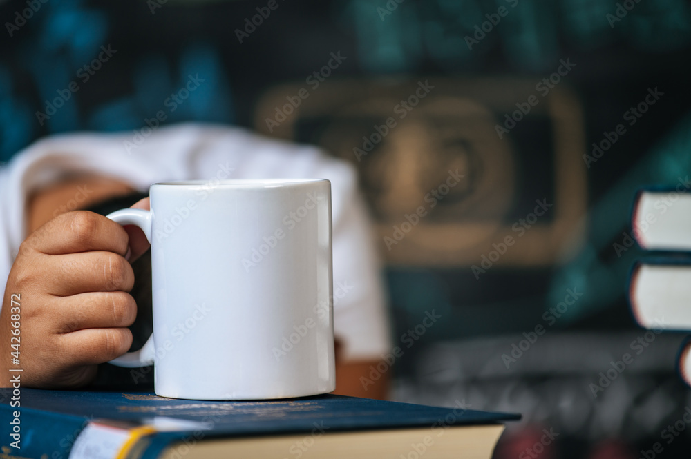 The hand was picking up the cup on top of the book in the classroom. The hand was picking up the cup on top of the book in the classroom.