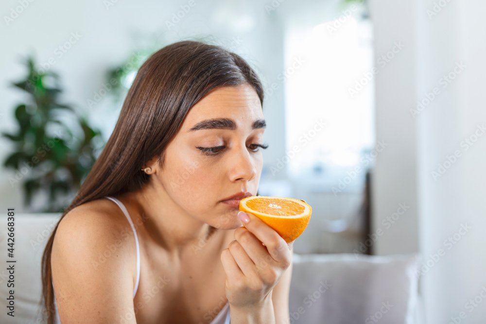 Sick woman trying to sense smell of half fresh orange, has symptoms of Covid-19, corona virus infection - loss of smell and taste. One of the main signs of the disease. Sick woman trying to sense smell of half fresh orange, has symptoms of Covid-19, corona virus infection - loss of smell and taste. One of the main signs of the disease.