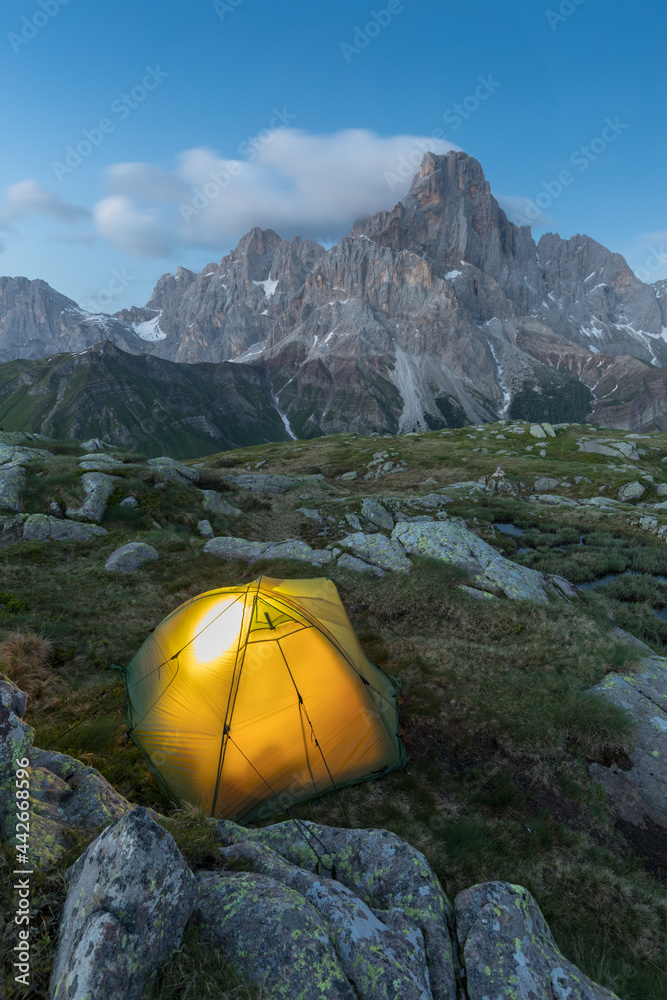 Dusk in mountain landscape with illuminated tent. Mountain peaks, Dolomites, Italy. Illuminated tent high in the mountains under the night sky 
Hiking and climbing concept