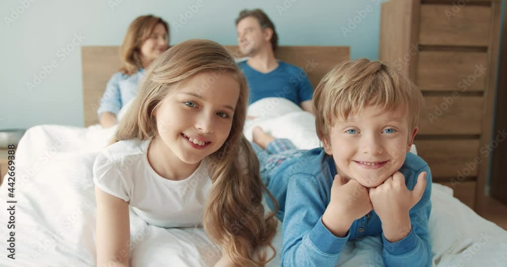 Portrait of happy little brother and sister lying on bed in the morning near their parents and smiling posing for camera. Portrait of happy little brother and sister lying on bed in the morning near their parents and smiling posing for camera.
