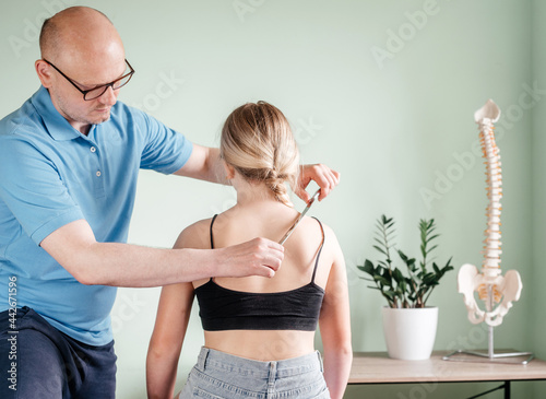 Osteopath practitioner performing fascia release maniupulations using IASTM treatment, girl receiving soft tissue treatment on her neck with stainless steel tool photo