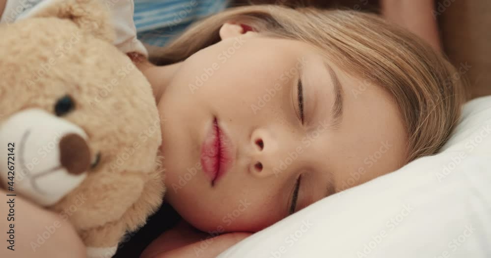 Close up of little Caucasian school girl falling asleep in bed in morning hugging her favorite soft toy.