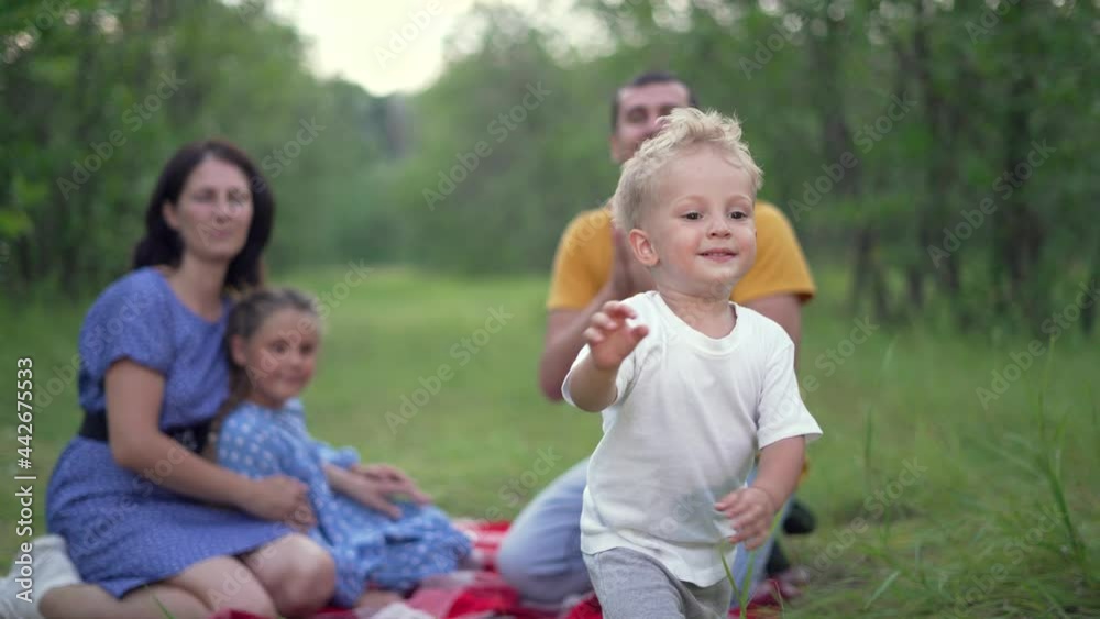 Happy family. Baby play with his parents in forest park. Family picnic on green grass in park. Baby run on green grass in forest. Happy family concept. People on picnic in park. Happy baby run Happy family. Baby play with his parents in forest park. Family picnic on green grass in park. Baby run on green grass in forest. Happy family concept. People on picnic in park. Happy baby run