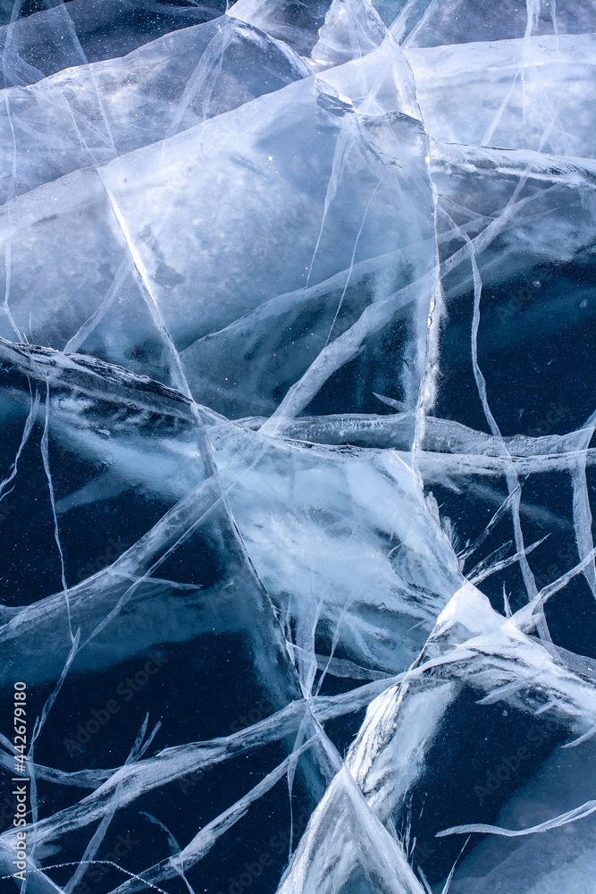 White deep cracks in transparent clear ice. Lake with blue ice. Vertical. White deep cracks in transparent clear ice. Lake with blue ice. Vertical.