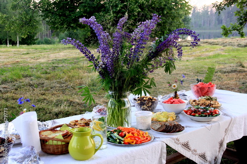 Midsummer food table.Table filled with drinks and food outside in the garden under the trees. on the table a glass vase with blue meadow flowers. Latvian LIGO festive