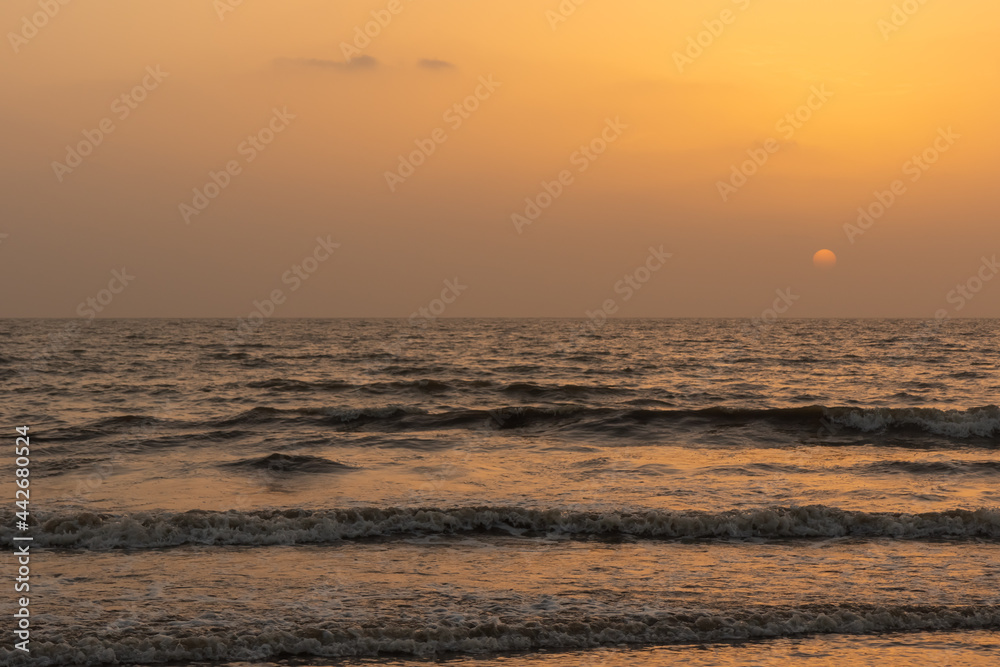 A view of the orange glow in the sky with sun setting in the horizon and waves in the ocean 