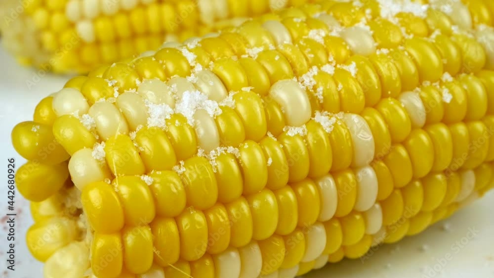 Sweet hot corn sprinkled with salt and ground red pepper. Grains of salt fall on hot corn and and ground chili. Mexican food. Close-up. Sweet hot corn sprinkled with salt and ground red pepper. Grains of salt fall on hot corn and and ground chili. Mexican food. Close-up.