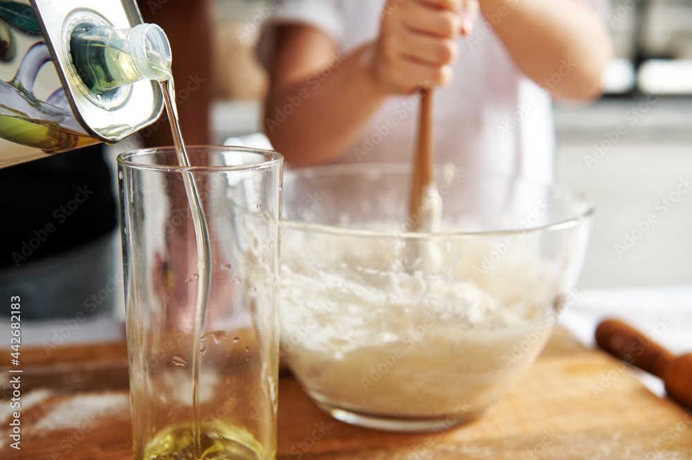 Close-up of pouring olive oil into a glass on a blurred background of a girl kneading dough Close-up of pouring olive oil into a glass on a blurred background of a girl kneading dough
