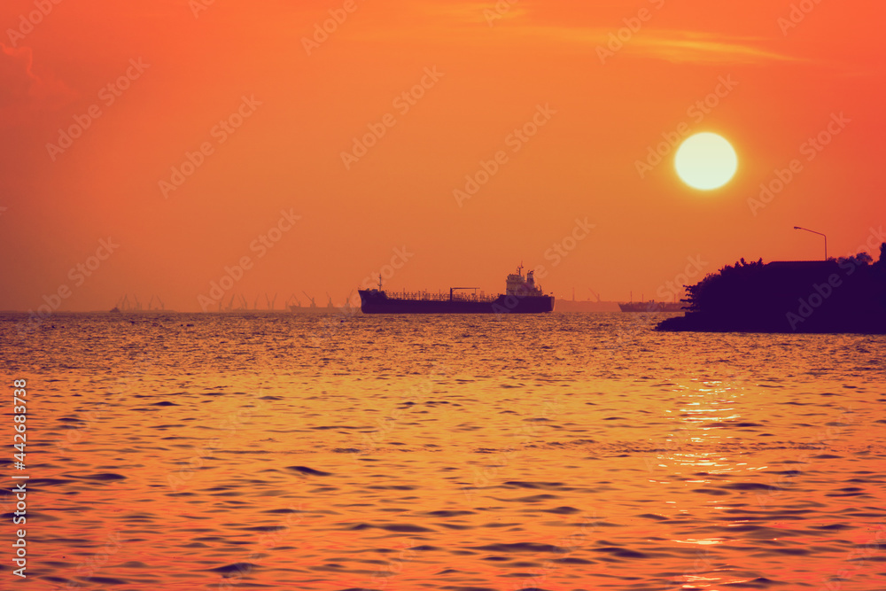 silhouette of marine cargo ship is anchored by the sea at sunset