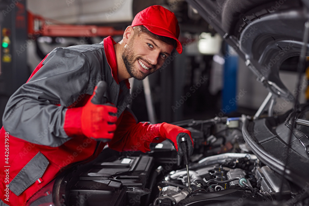 Fototapeta premium Cheerful mechanic showing thumb up while repairing car engine