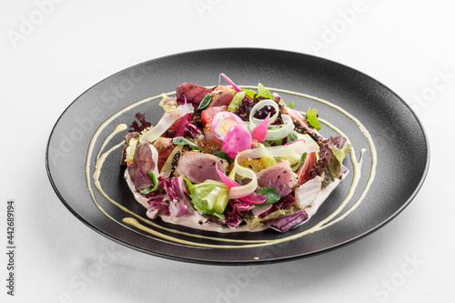 healthy green salad with seared tuna and orange on black plate isolated on white background