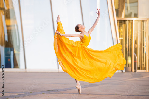 young ballerina in a long flying yellow dress is dancing against the backdrop of cityscape