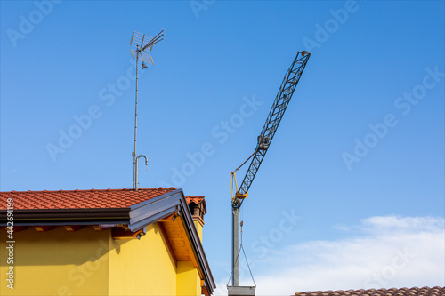 Gru per il sollevamento di materiali da costruzione sopra il tetto delle case ristrutturate con antenna per la ricezione di programmi televisivi. Giornata estiva con cielo sereno. photo