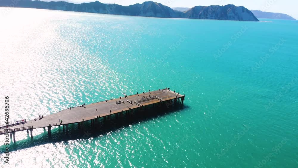Long wharf at Tolaga Bay, Aerial shot of people enjoying a walk during sunny day. New Zealand coastal scenery reveal.
