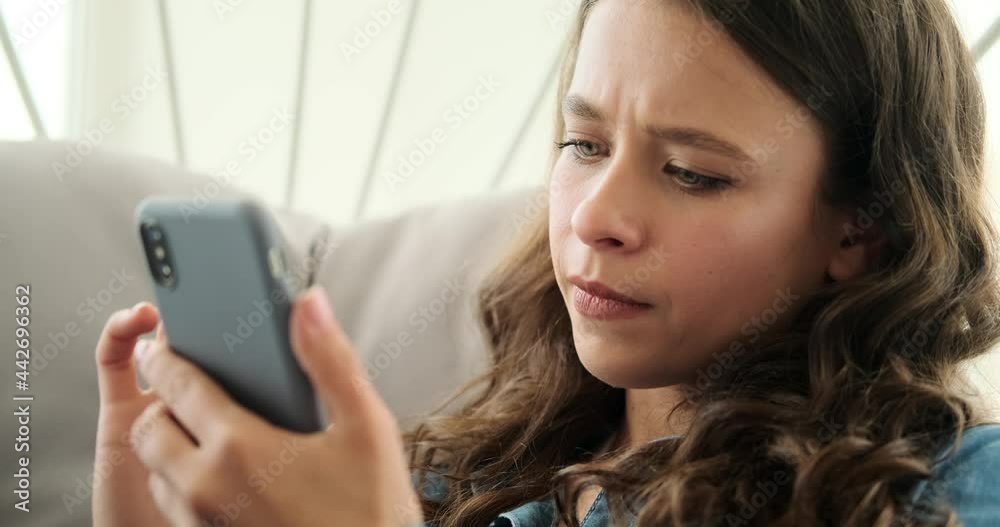 Serious woman text messaging on mobile phone sitting on luxury chair at home