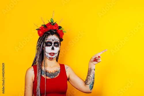 Woman with sugar skull makeup show near her on yellow background, Day of the dead