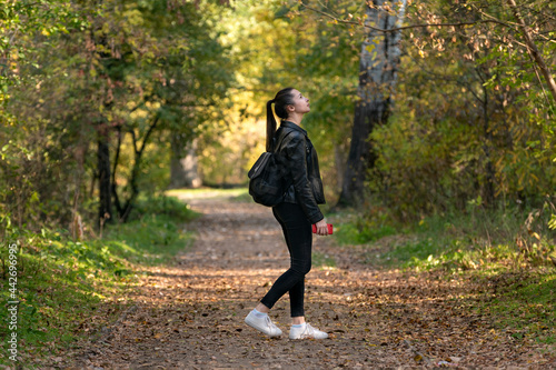 Girl student walks in the autumn park. Stylish young woman walks in the forest. Alley with yellow fallen leaves.