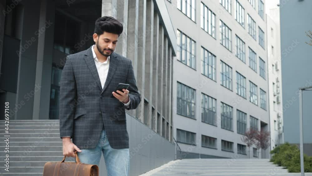 Stylish arabian man in business clothes standing near office center and using modern smartphone. Bearded businessman with suitcase in hands surfing internet outdoors Stylish arabian man in business clothes standing near office center and using modern smartphone. Bearded businessman with suitcase in hands surfing internet outdoors