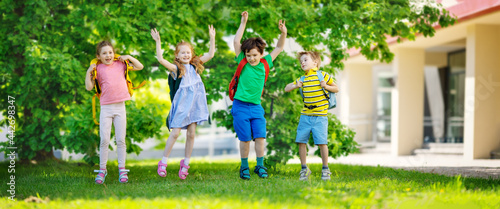 Cute children with rucksacks jumping and playing in the park near the school