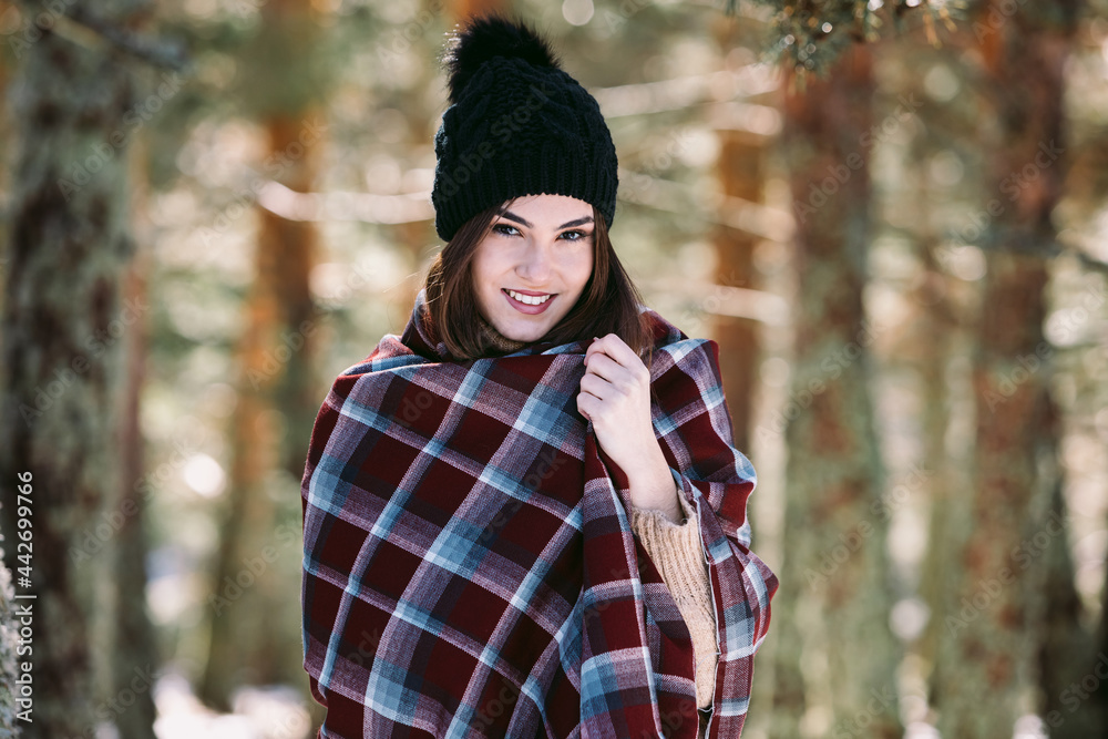 Smiling woman wrapped in blanket standing in winter forest Smiling woman wrapped in blanket standing in winter forest