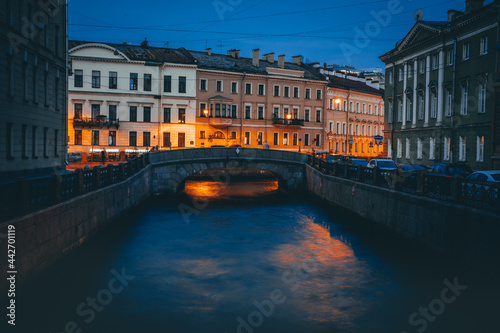 Beautiful view of the street illuminated by lights and the canal between the buildings at night in St. Petersburg. Long-exposure photo