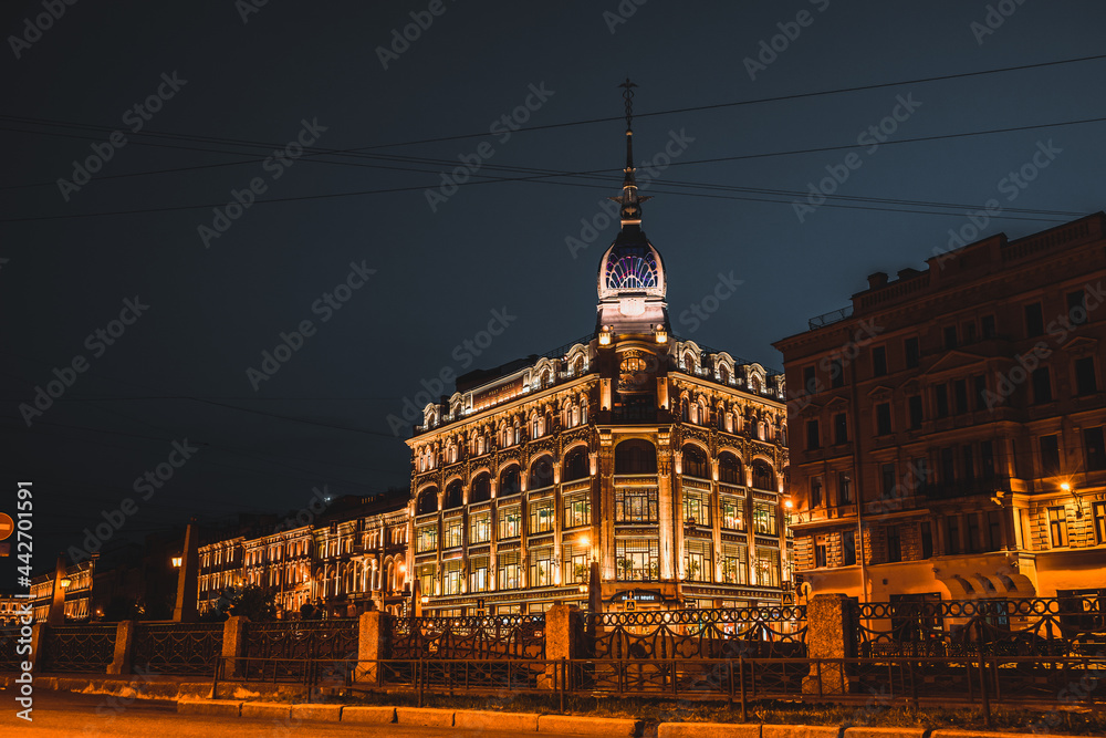 View of the landmark of St. Petersburg, a beautiful historical building next to the red bridge near the river channel at night. Saint Petersburg, Russia - 22 June 2021