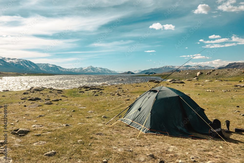 Tourist tent in camp among meadow in the mountains and lake. Camping hiking lifestyle.