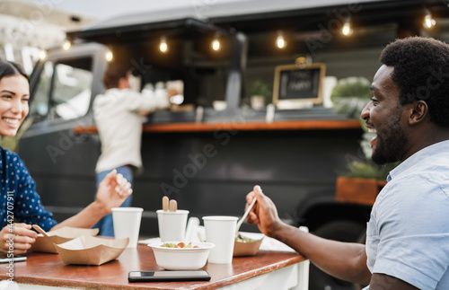 Multiracial people having fun eating at food truck restaurant outdoor - Focus on african man face