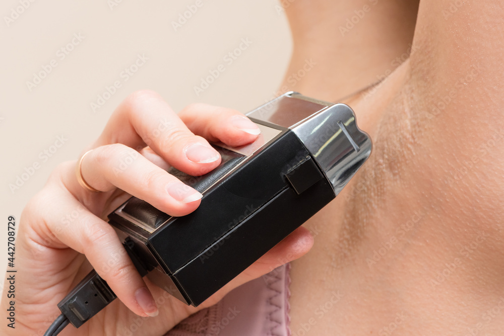 Fototapeta premium Woman is shaving an underarm with electric razor close up.