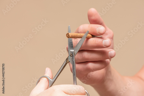 Male hand with a cigarette and woman hand with a scissors cuts a cigarette close up.